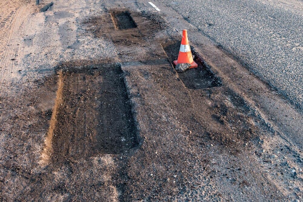 Drum asfaltat cu reparații în desfășurare și utilaje pentru asfaltare, într-o zonă rurală.