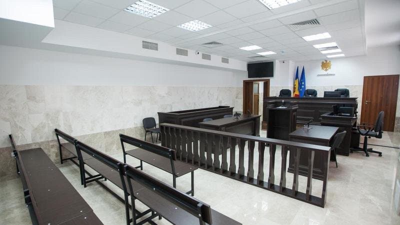 Laptop pe o masă dintr-o sală de judecată, folosit pentru o ședință prin videoconferință