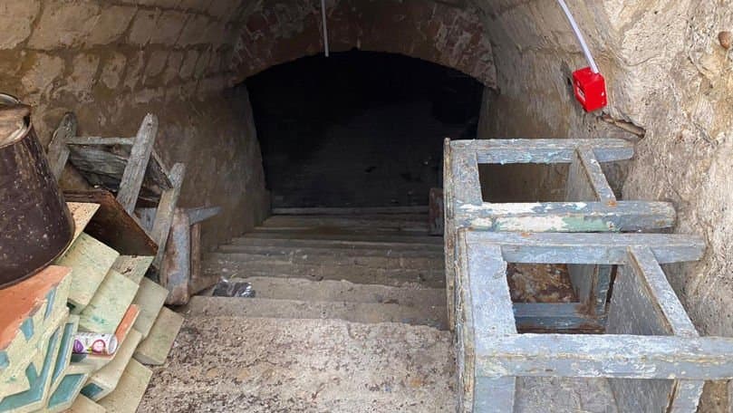 Intrare de beton într-un adăpost subteran vechi de protecție civilă, cu ușă metalică ruginită