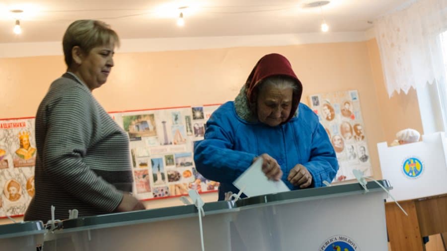 Urnă de vot transparentă și buletine de vot pe o masă, într-o secție de votare