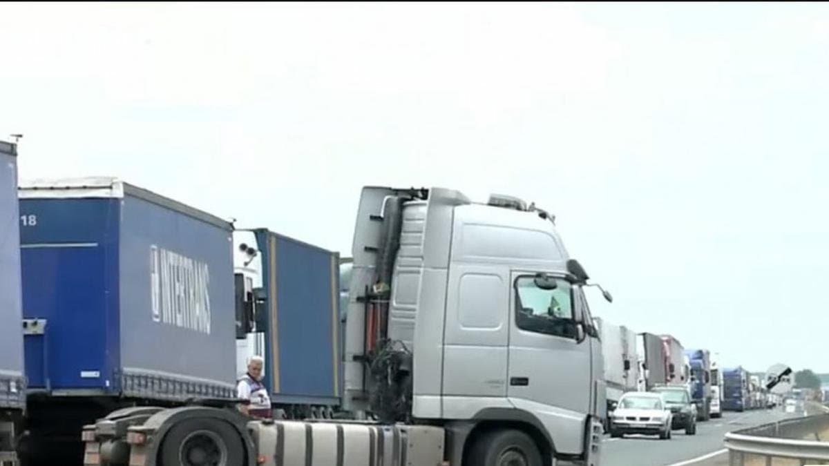 Șir lung de camioane care așteaptă pe drum, aproape de un punct vamal