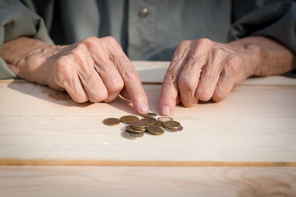 Mâinile unui pensionar care numără bancnote la o masă